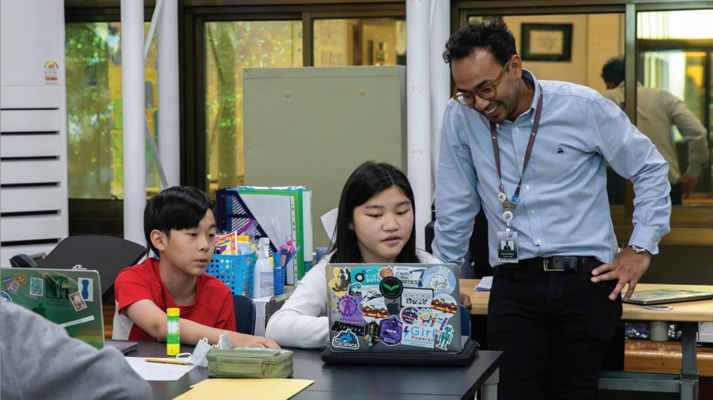 Rafael leaning in to help two students working at a laptop.